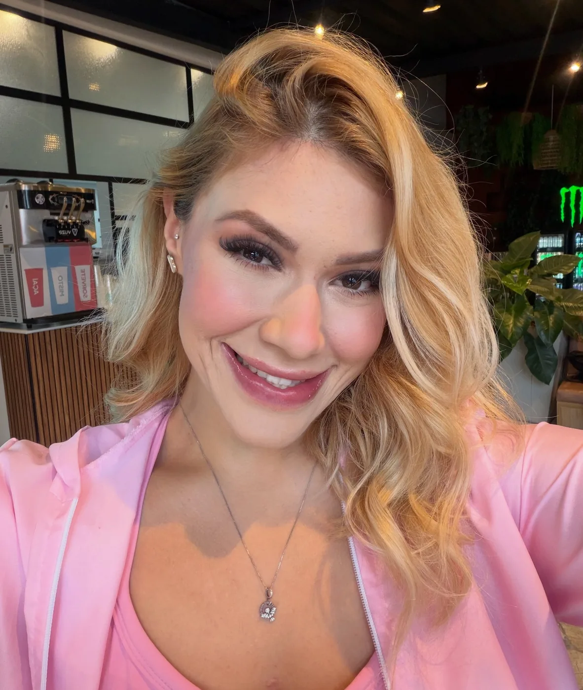 Close de Bre Cardoso sorrindo, de blazer rosa e cabelo loiro platinado