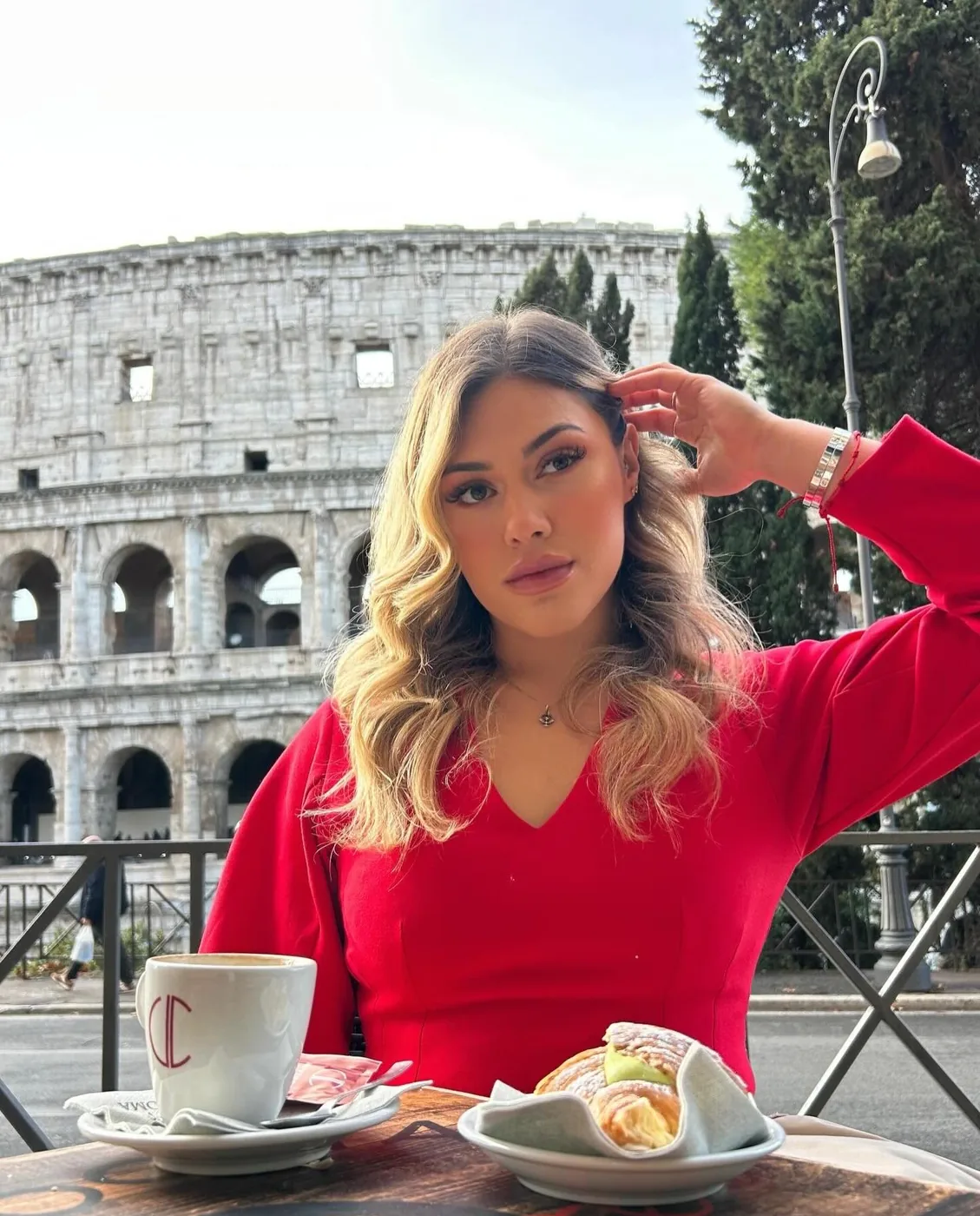 Bre Cardoso de blusa vermelha num café com o Coliseu de Roma ao fundo